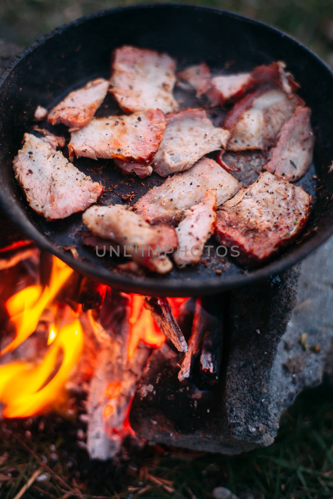 Slices of fried bacon in a pan. Food in a forest camp. Cooking o by Opikanets
