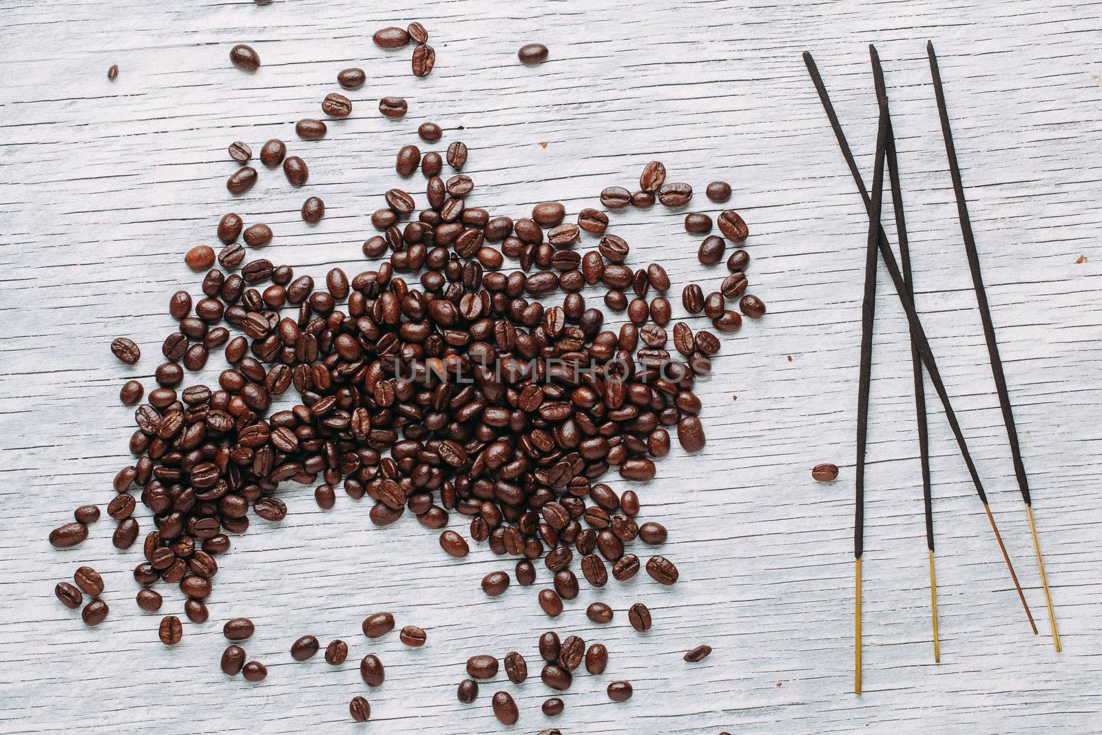 A scattering of coffee beans on a white wooden background with aromatic sticks.