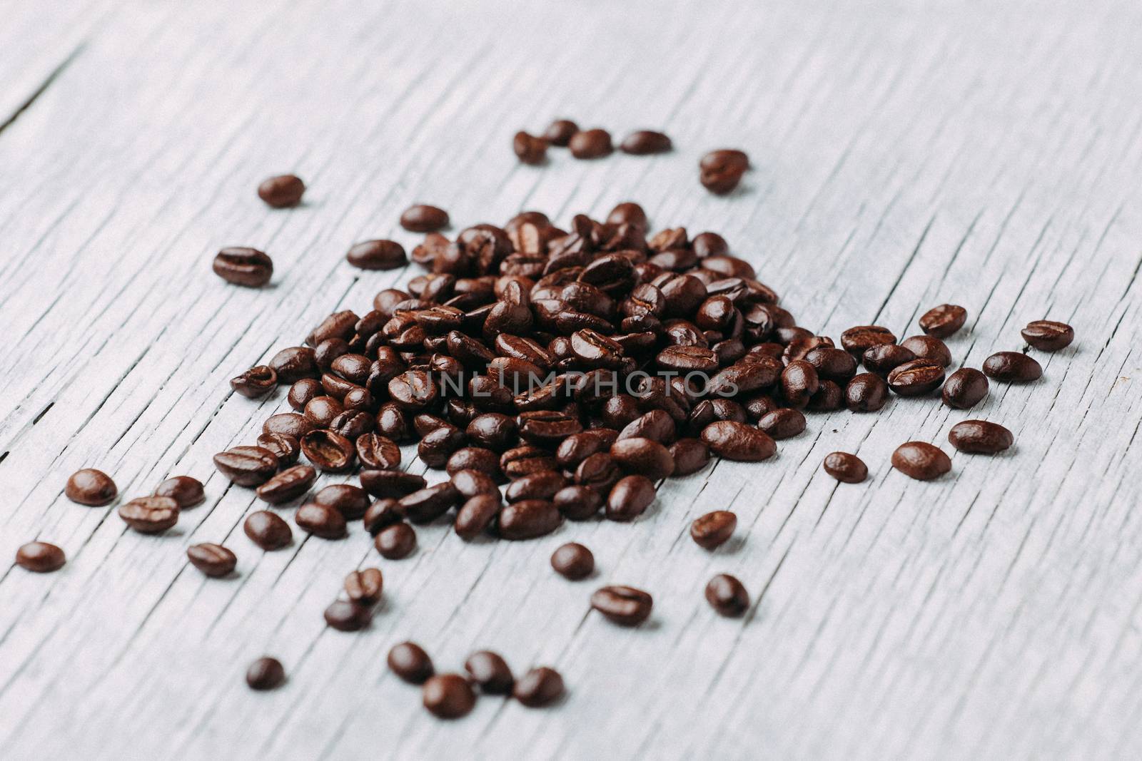 A scattering of coffee beans on a white wooden background.