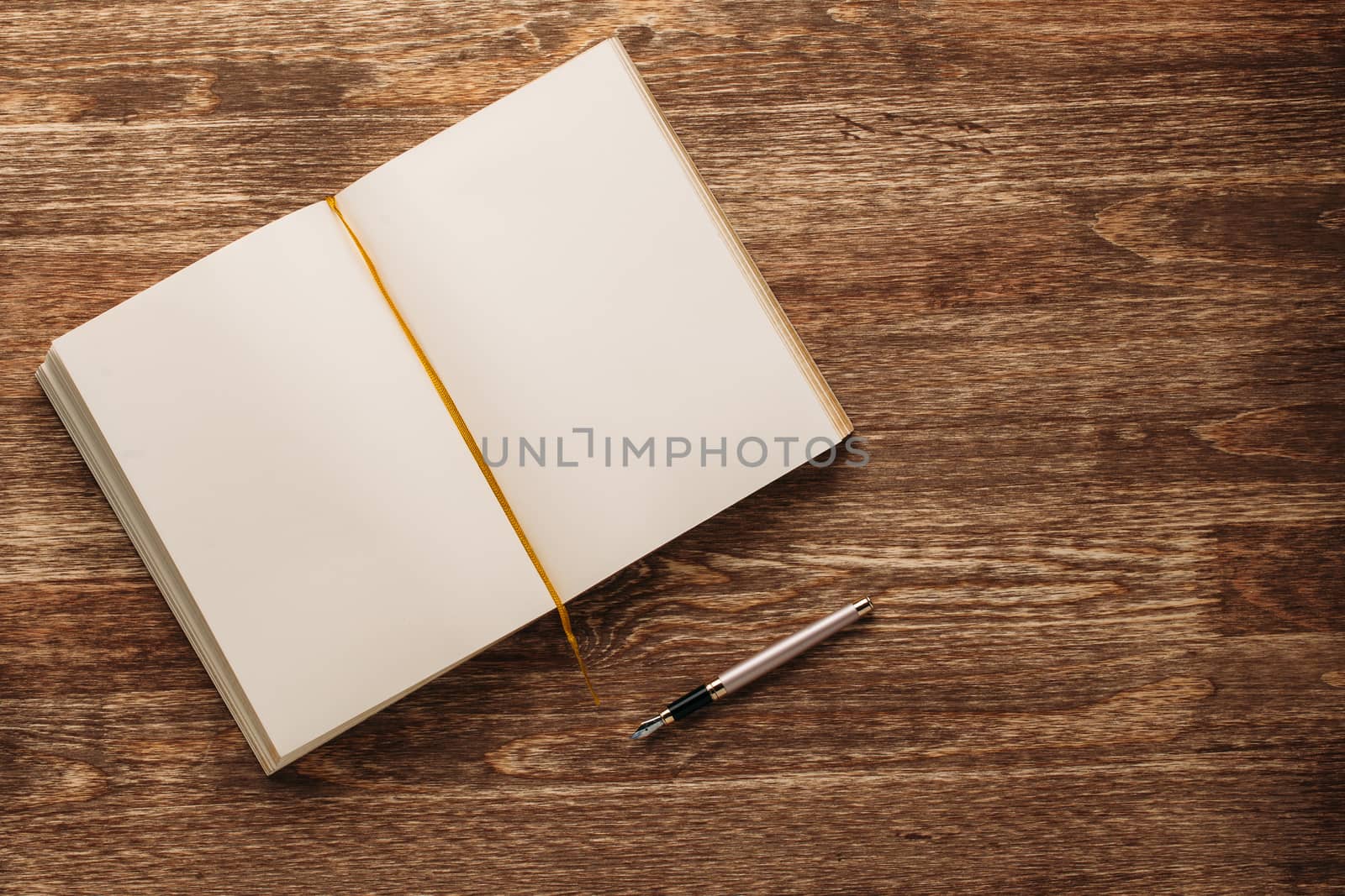 Open notebook with yellow blank pages and fountain pen on a wooden background.