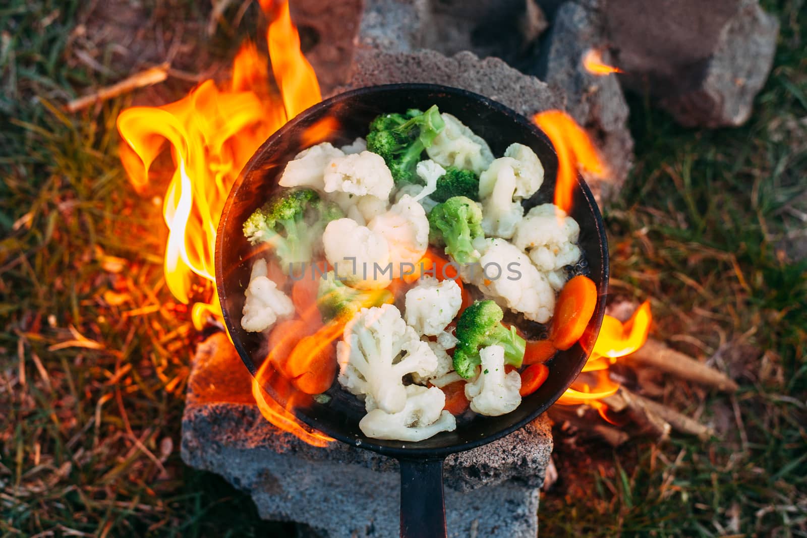 Cauliflower, broccoli and carrot in a pan. Cooking on an open fire. Outdoor food. Grilled vegetables. Food on a camping trip