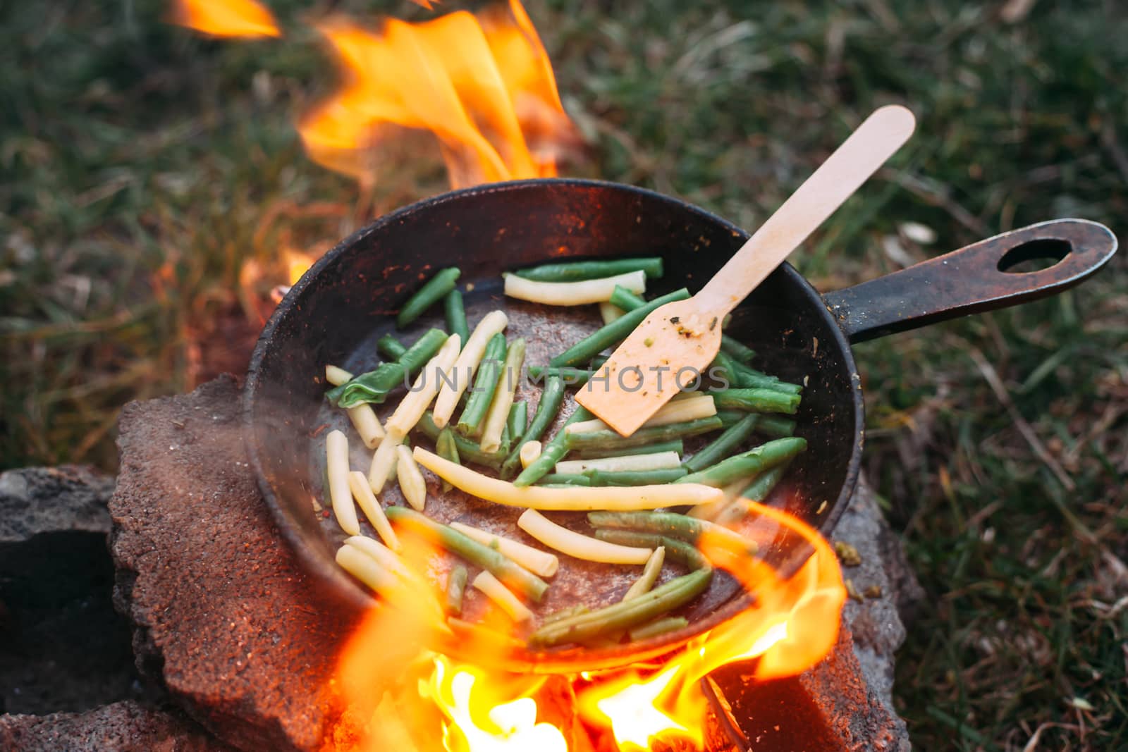String beans in a pan. Cooking vegetables on an open fire. Food on a camping trip. Wooden spatula in a pan