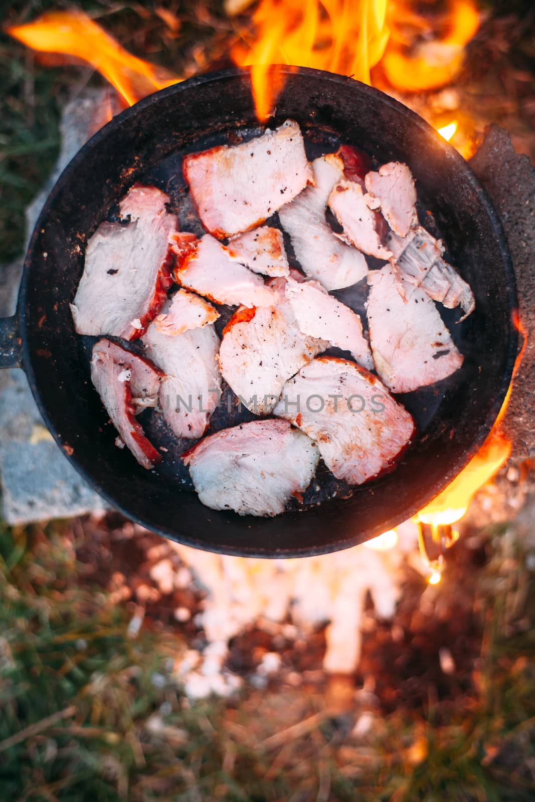 Slices of fried bacon in a pan. Food in a forest camp. Cooking o by Opikanets