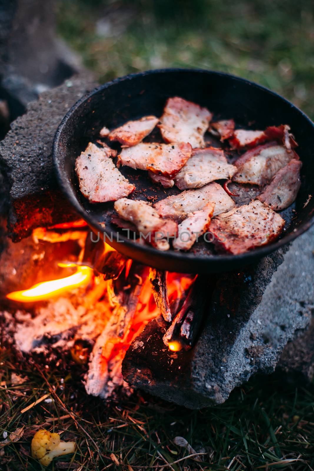 Slices of fried bacon in a pan. Food in a forest camp. Cooking on fire. Picnic in the nature. Grilled food on nature.