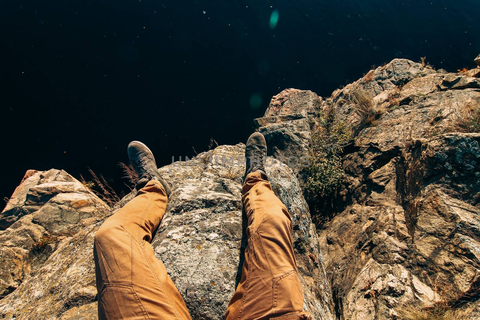 Man sitting on a rock. Photo of feet on a background of water. A by Opikanets