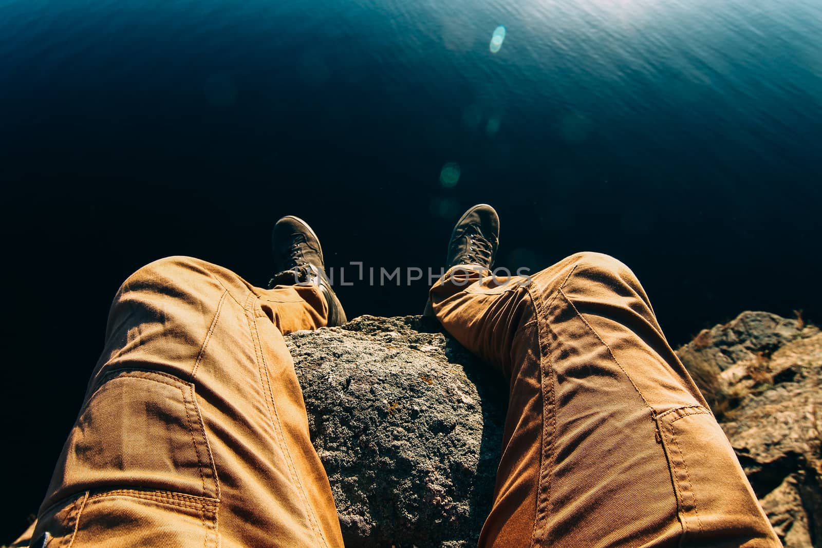 Man sitting on a rock. Photo of feet on a background of water. A by Opikanets