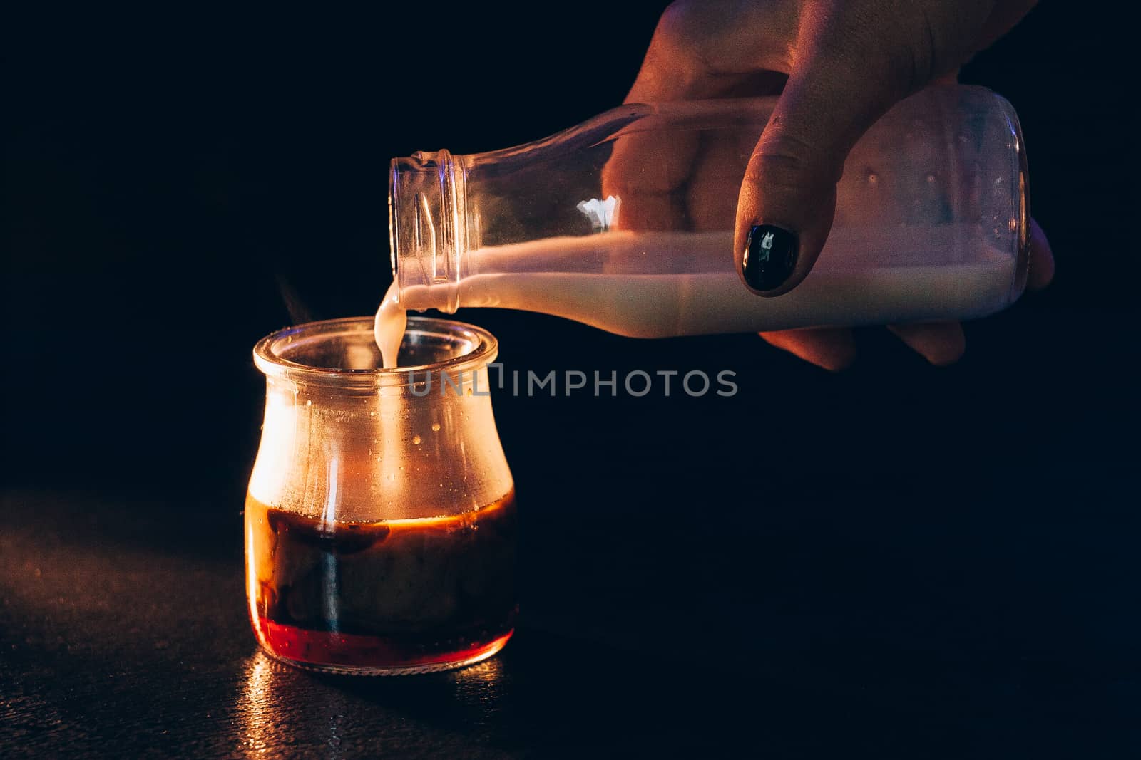 Girl pours milk from a bottle into a jar of coffee on a dark background with warm light