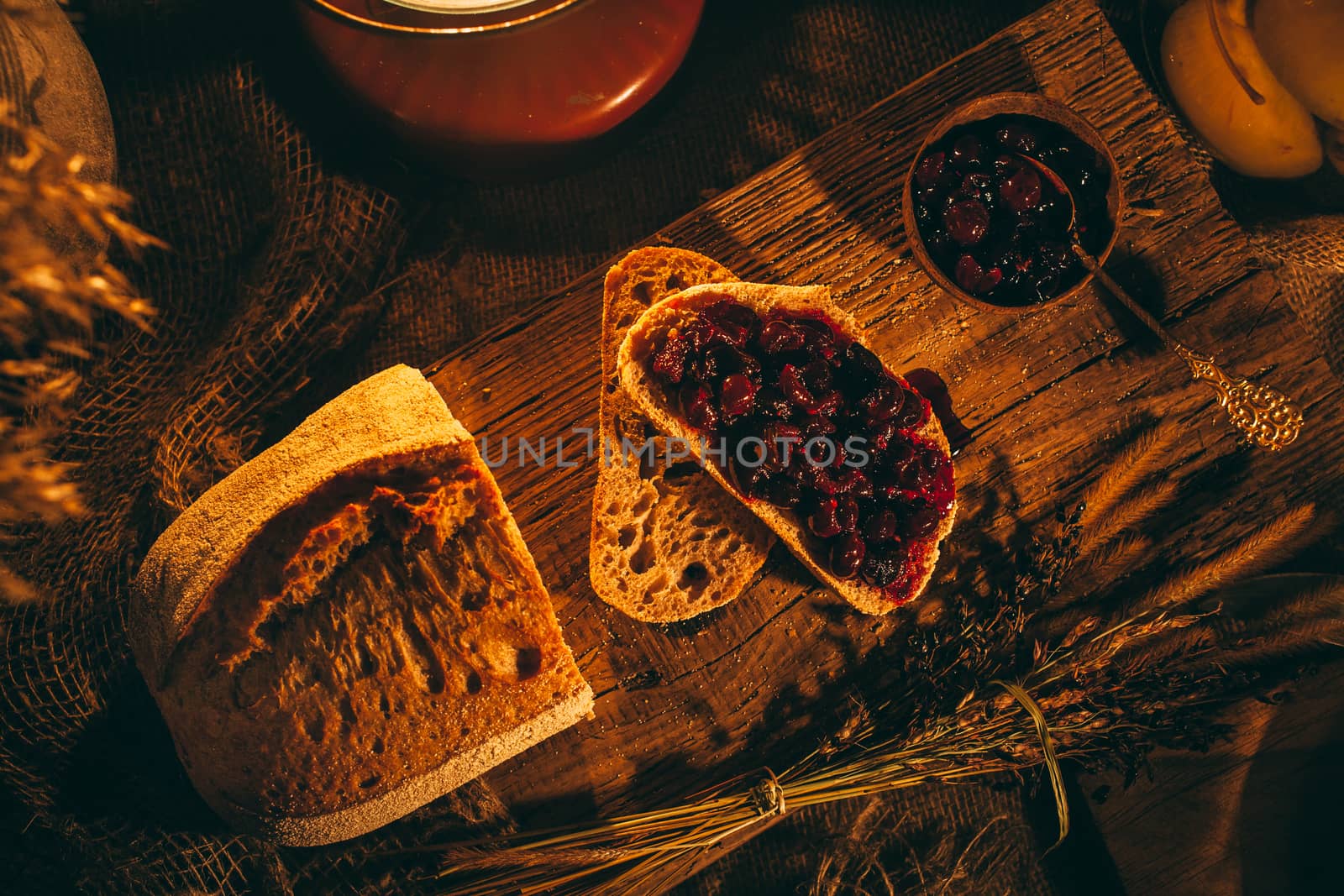 Sliced ​​bread with jam in the light of candles on a wooden board. Rustic atmosphere.Photo from the top