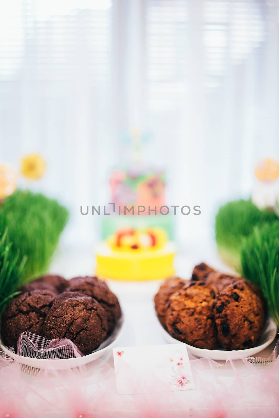 Festive table with a large cake with mastic flowers. Candy bar with grass on which a cake with cookies and lollipops