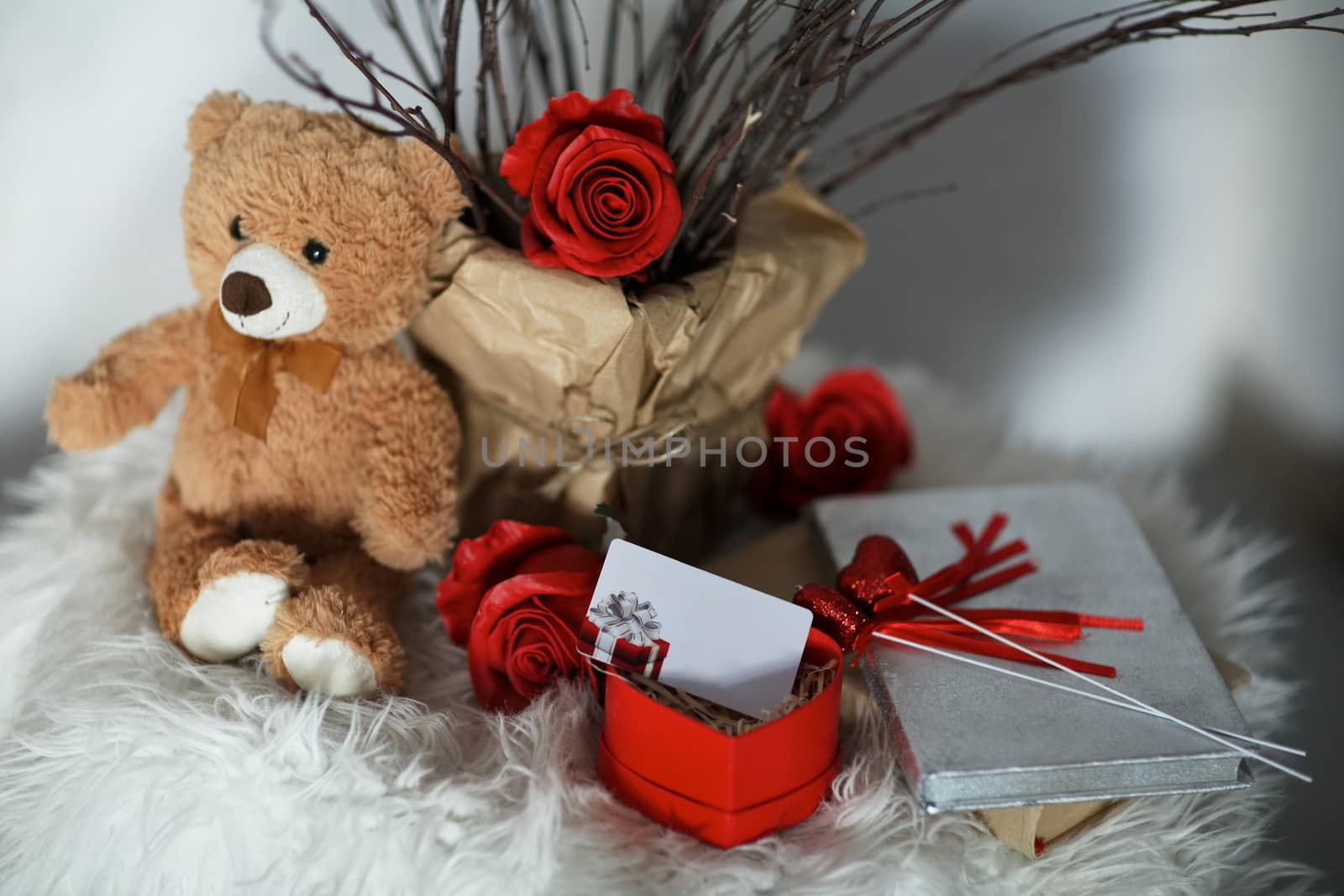 A bear with rose flowers on white skin on which a gift certificate in a box. A gift for Valentine's Day