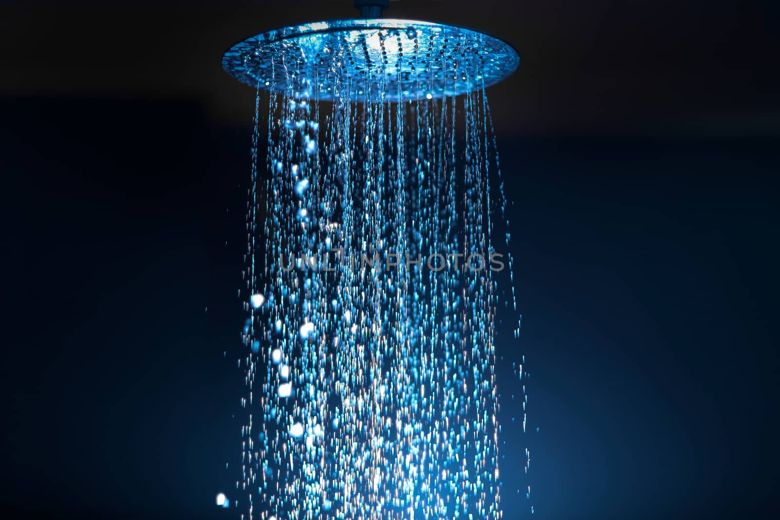 Water falling from the shower on a dark background with blue backlight in the aqua zone