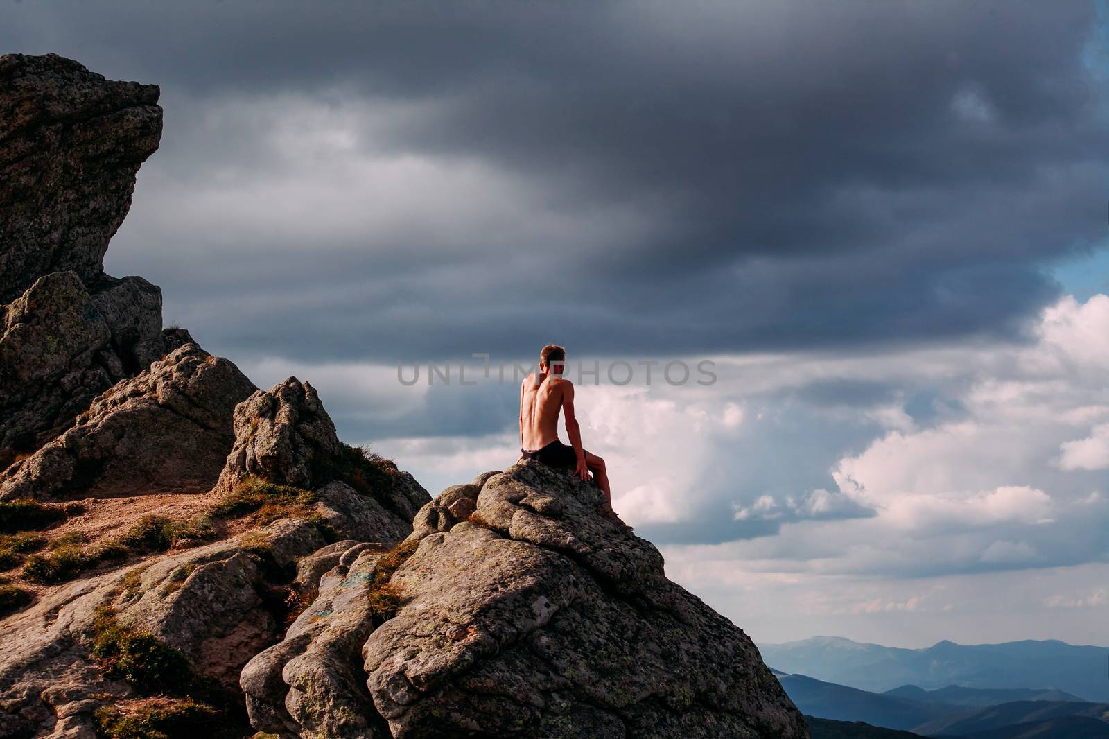 A guy sits on a stone in the mountains and looks into the distan by Opikanets