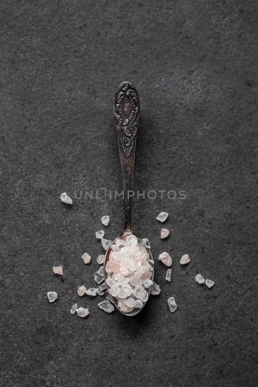 Spoon with Himalayan salt on a black table by Opikanets