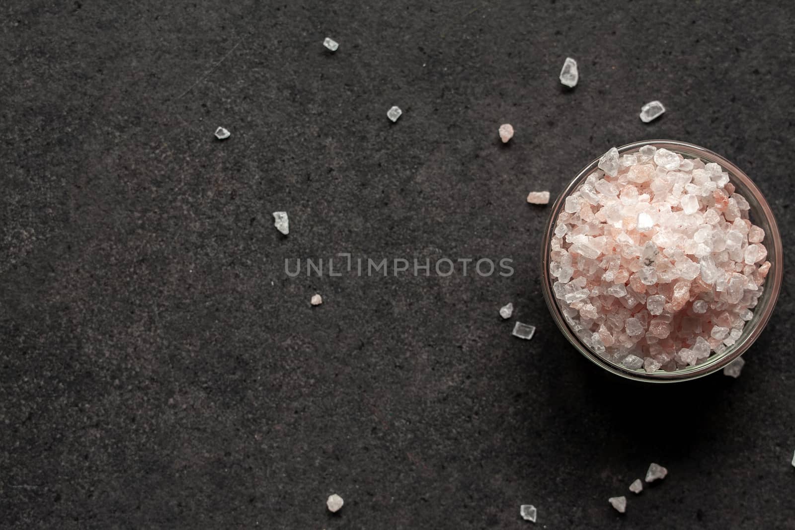 Spilled salt near a saucer full of Himalayan salt on a black slate board.With place for inscription.