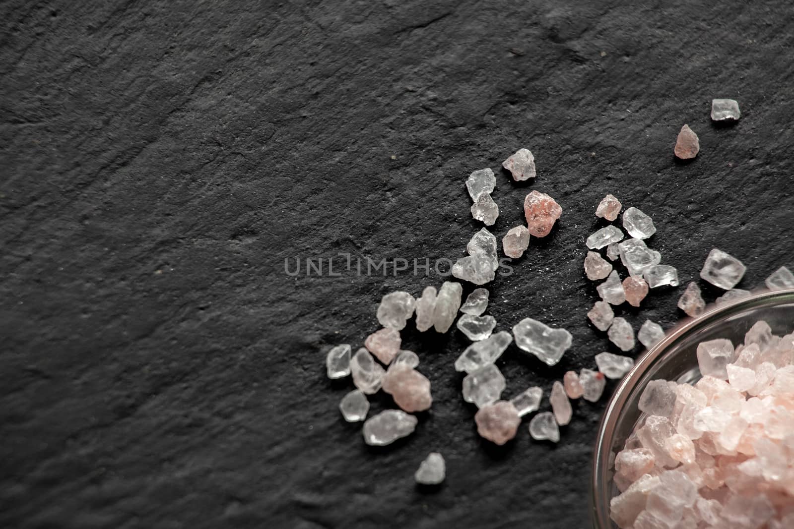 Spilled salt near a saucer full of salt on a black slate board by Opikanets