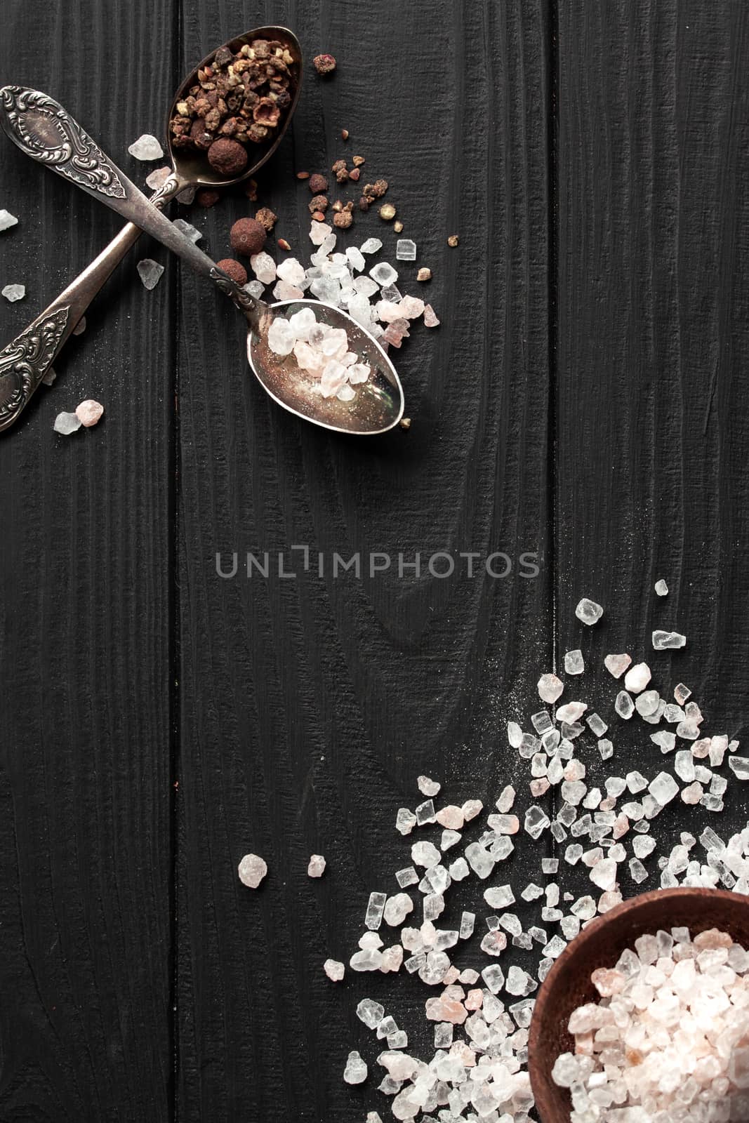 Spoons with Himalayan salt and seasonings on a black wooden background and a saucer with salt. With place for inscription