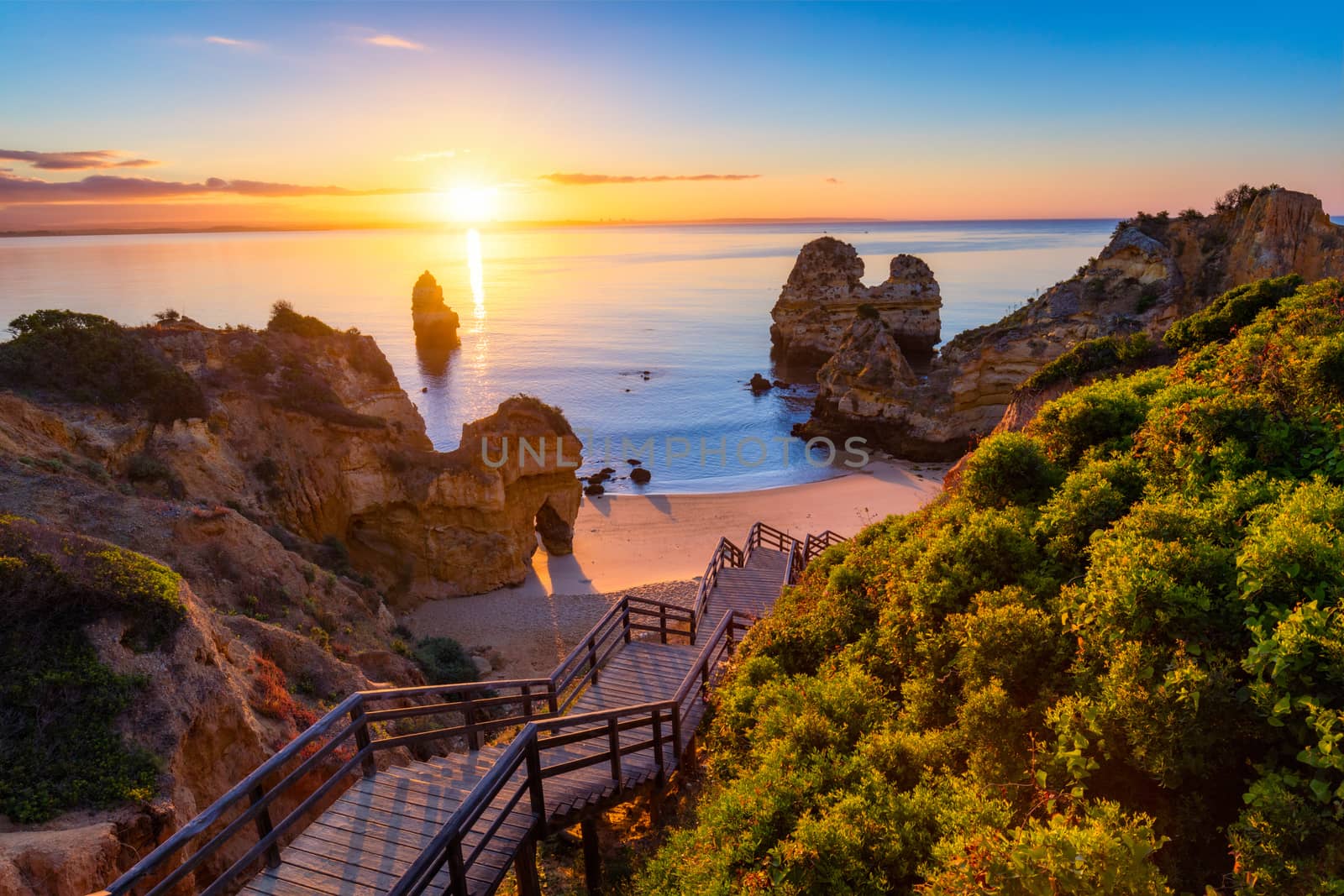 Sunrise at Camilo beach in Lagos, Algarve, Portugal. Wooden footbridge to the beach Praia do Camilo, Portugal. Picturesque view of Praia do Camilo beach in Lagos, Algarve region, Portugal.