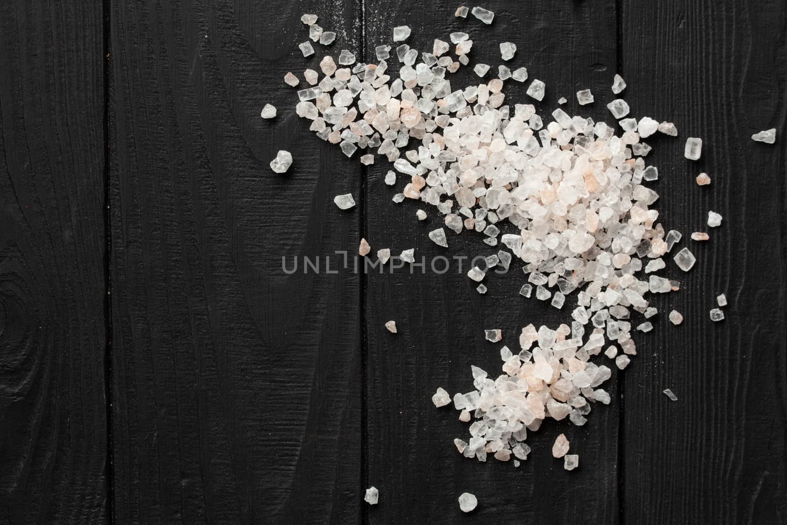 A scattering of pink Himalayan salt on a black wooden background by Opikanets