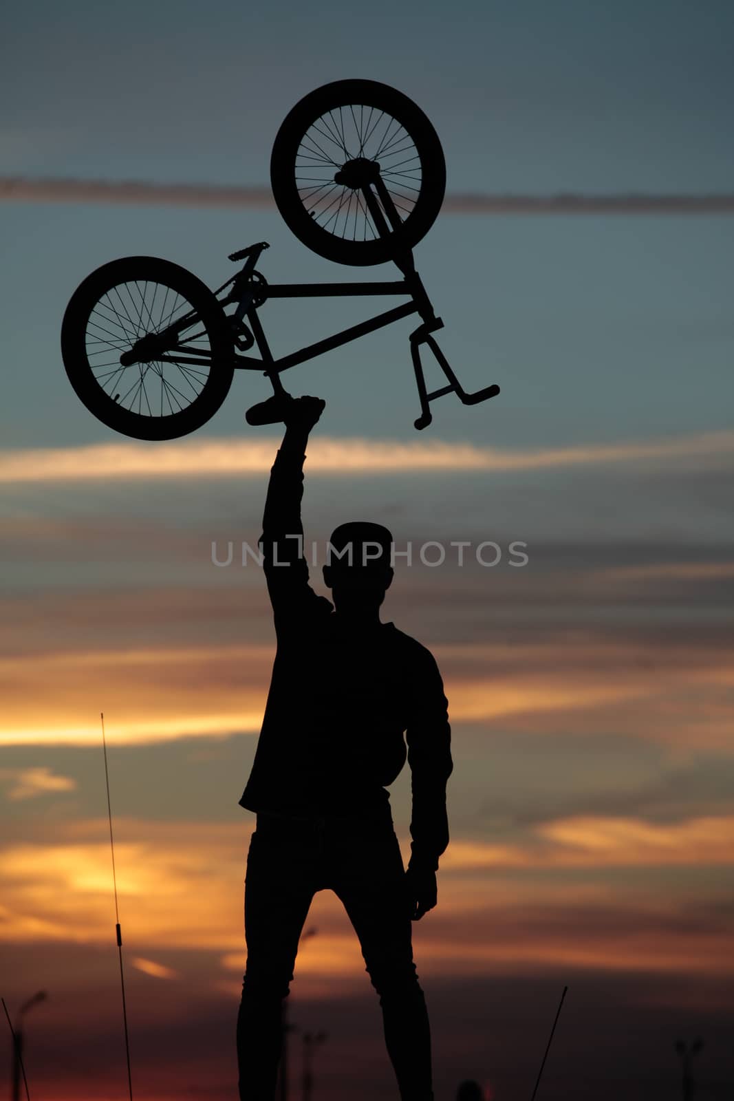 Silhouette of a cyclist holding his bike over his head on a suns by Opikanets