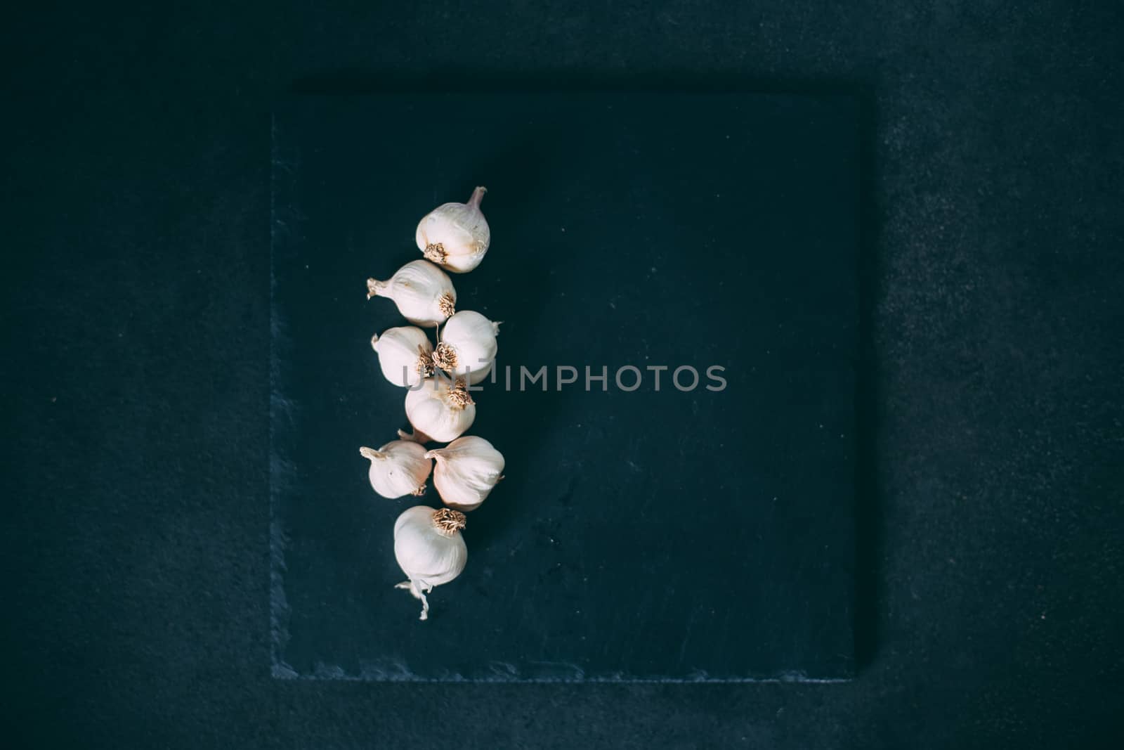 Garlic heads on a slate plate which lies on a black wooden backg by Opikanets