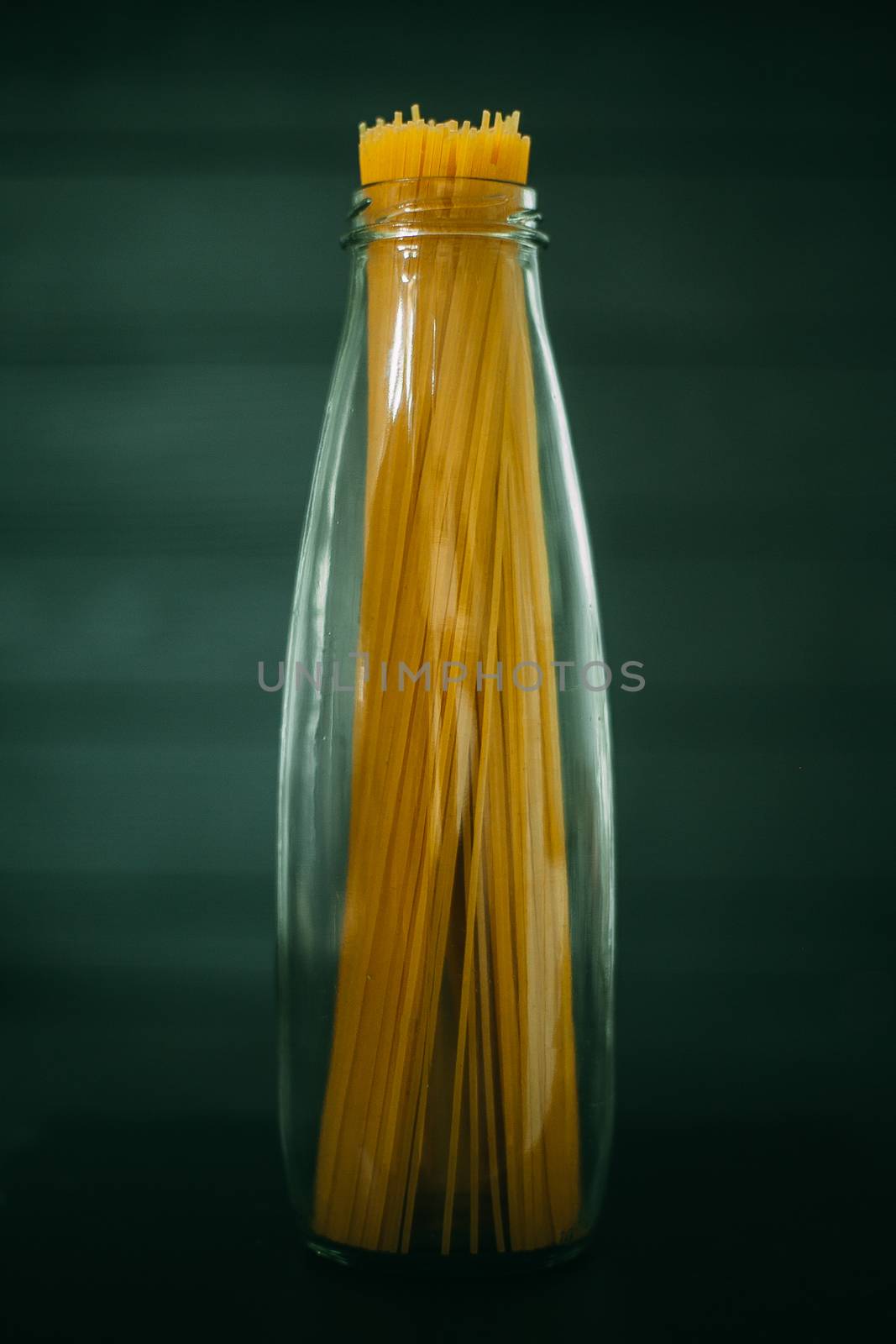 Spaghetti in a glass jar on a white tile background