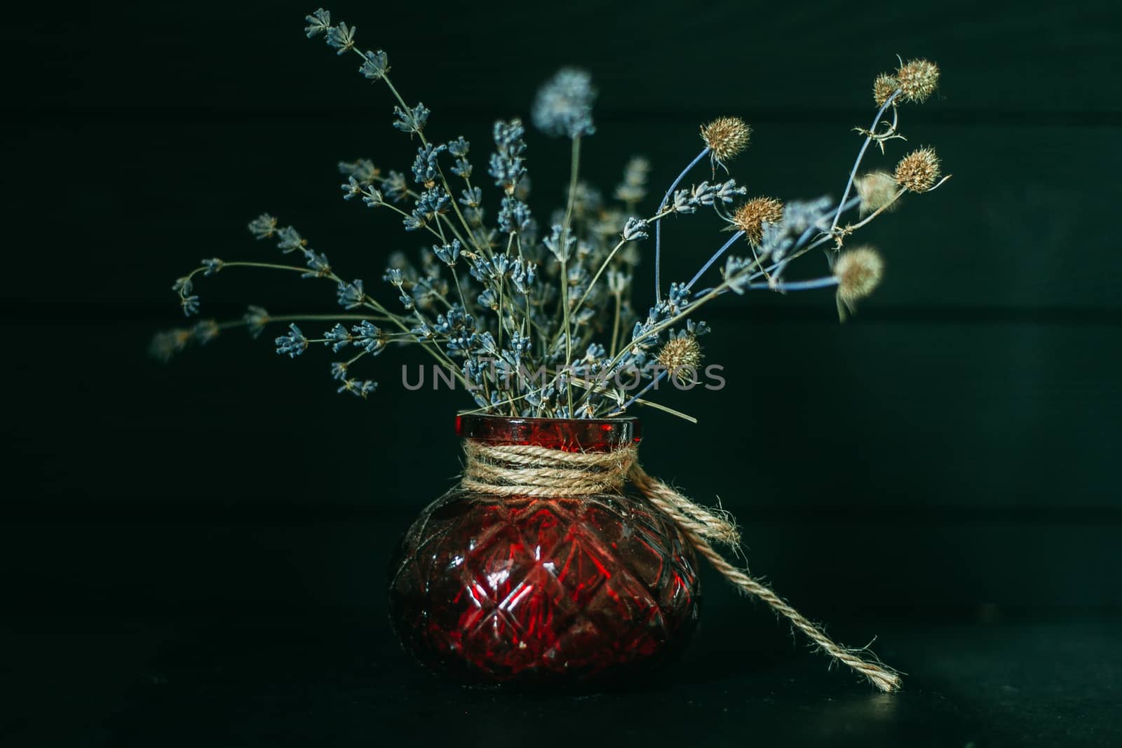 Dry bouquet with field plants in an old red vase on a wooden dark background