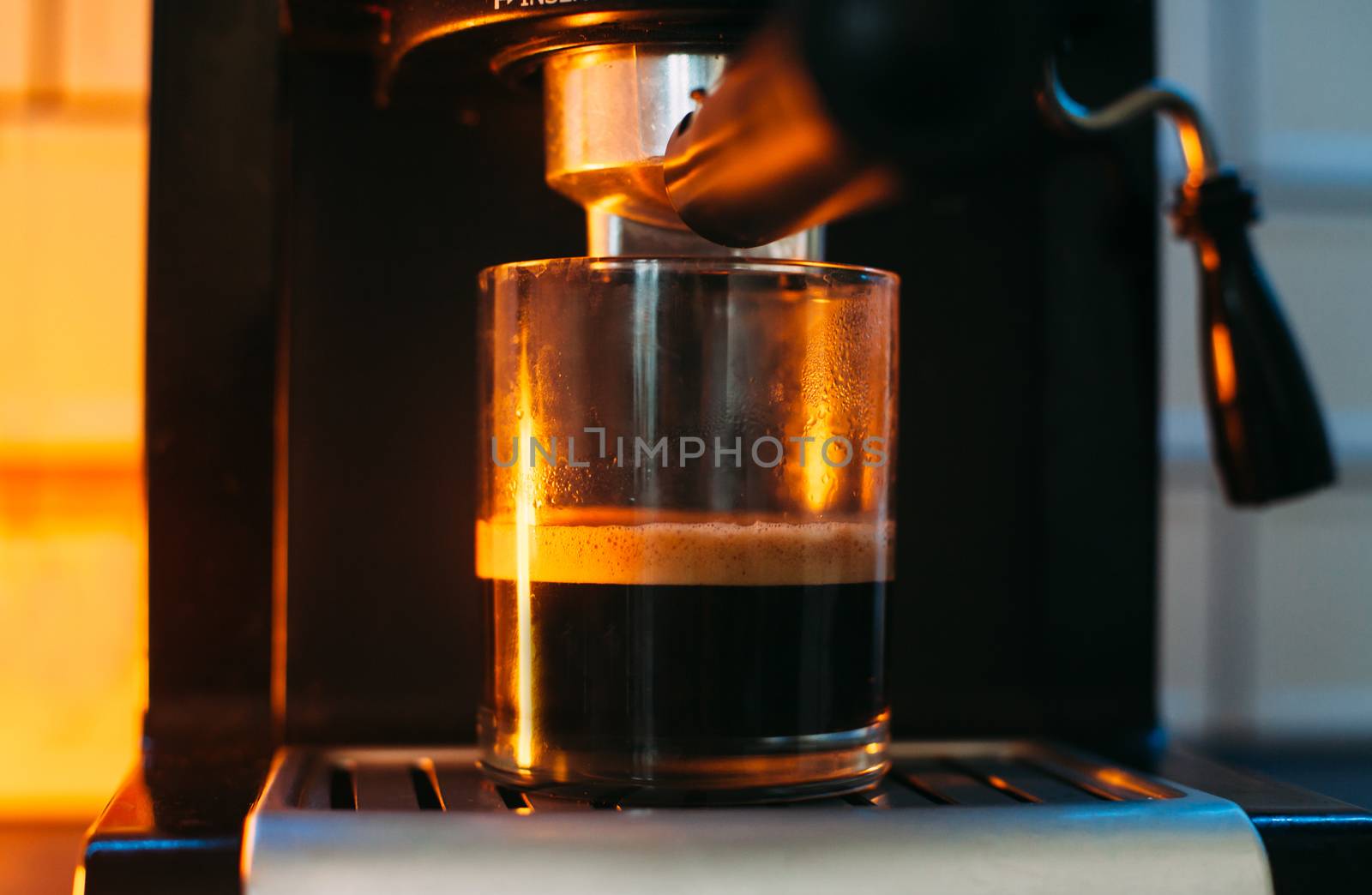 A filling glass is standing in a coffee machine with a yellow li by Opikanets