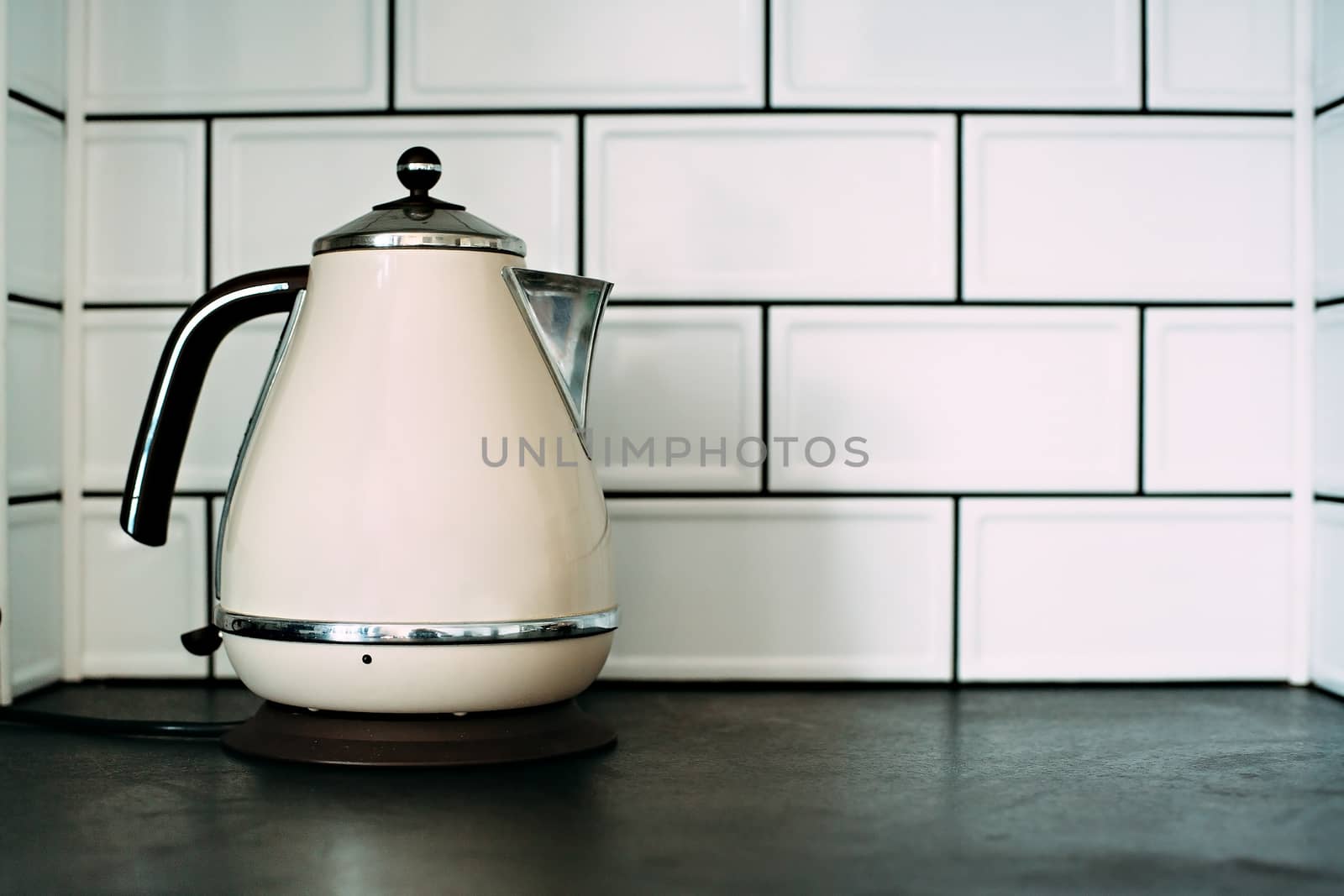 Metal electric kettle on a white tiled wall