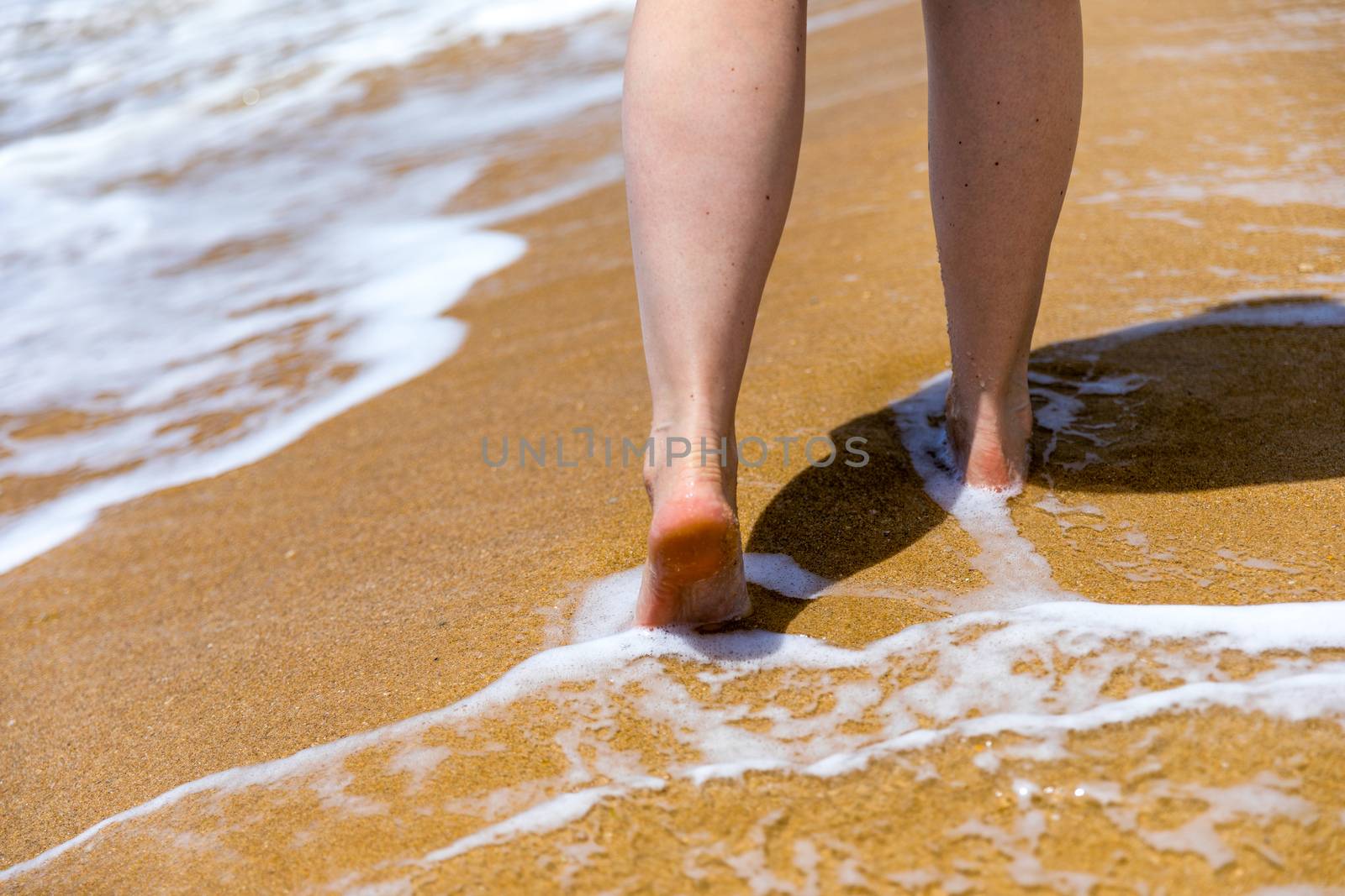 Woman walking barefoot on a beach. Close up leg of young woman walking along wave of sea water and sand on the summer beach. Travel Concept. Woman walking on sand beach leaving footprints in the sand.