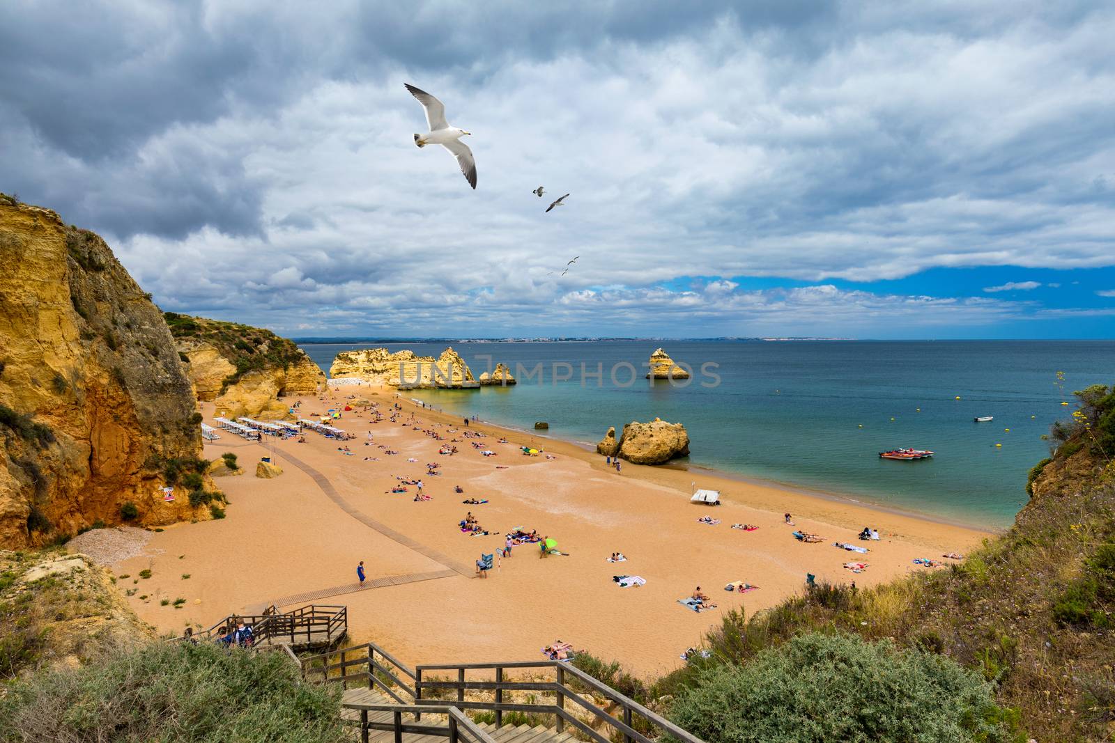 Wooden walkway to famous Praia Dona Ana beach with turquoise sea water and cliffs, flying seagulls over the beach, Portugal. Beautiful Dona Ana Beach (Praia Dona Ana) in Lagos, Algarve, Portugal.