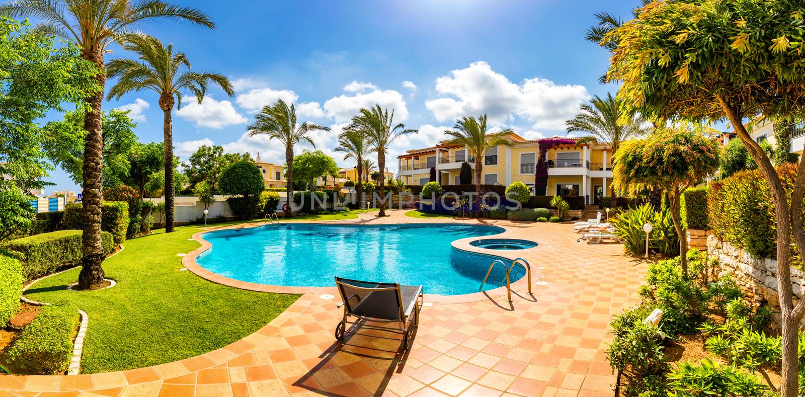 Swimming pool, sun-loungers and palm trees during a warm sunny day, paradise destination for vacations. Backyard swimming pool with garden full of palm trees and flowers. Backyard with swimming pool.