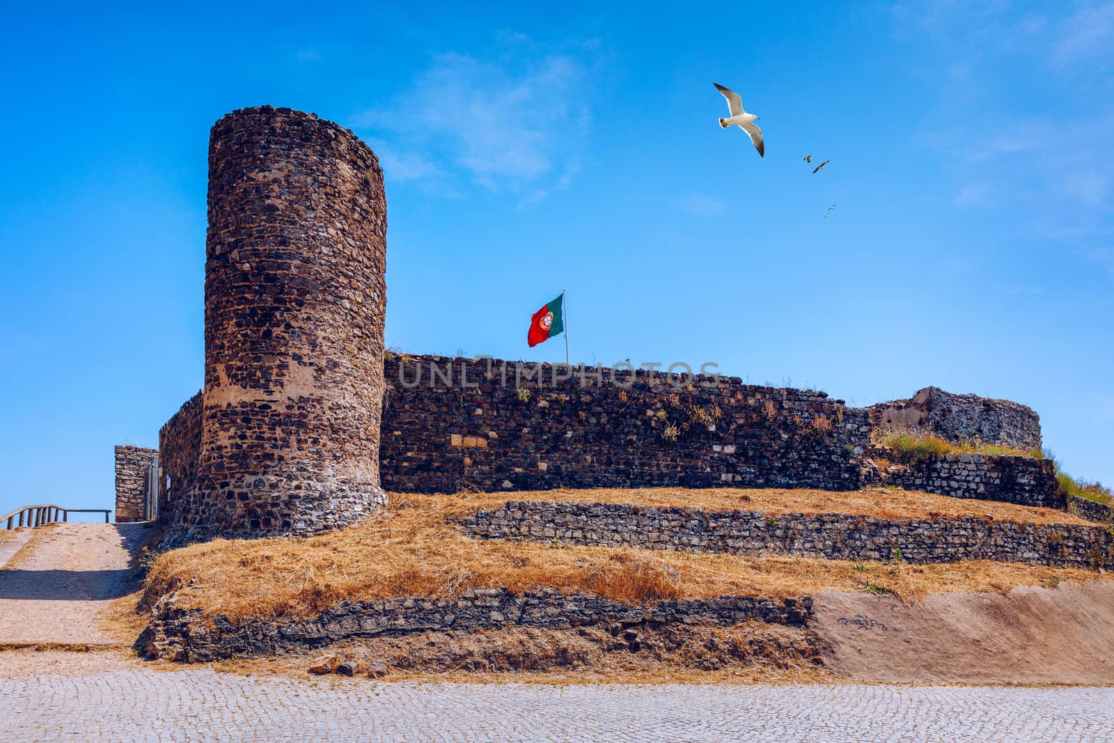Ruins of Castle in Aljezur with waving portuguese flag, Algarve, Portugal. Aljezur castle, Portugal Arabian gorgeous castle, made of stone with a tower. Aljezur, Algarve, Portugal.