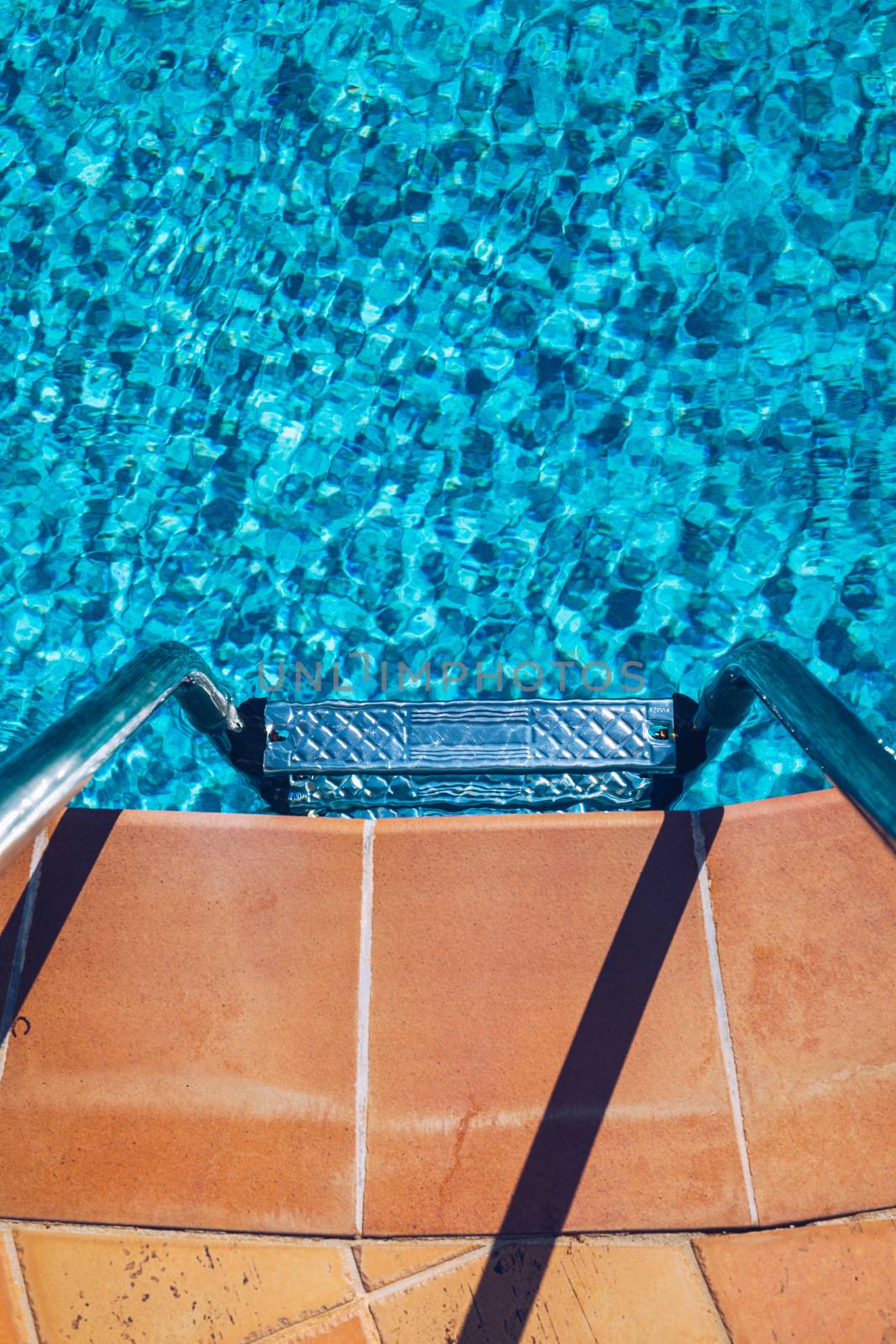 Swimming pool with stair. Grab bars ladder in the blue swimming pool. Poolside with blue clear water and ladder. Stair at the side of swimming pool, summer concept.
