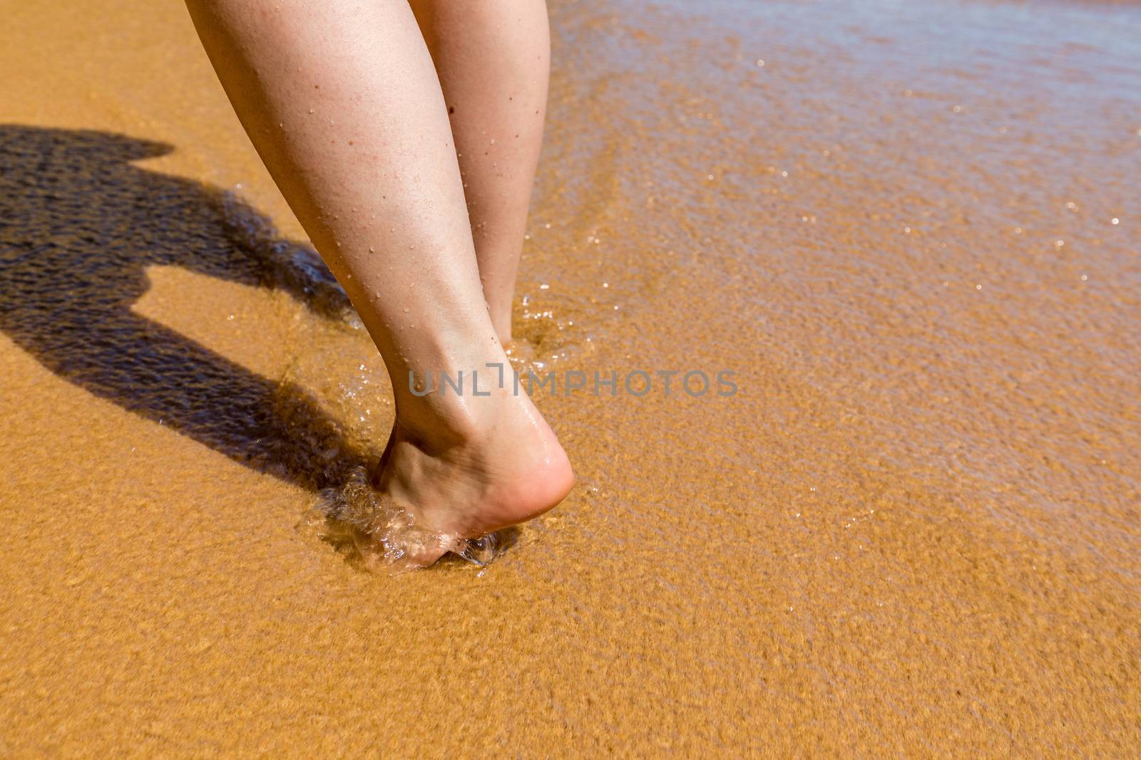 Woman walking barefoot on a beach. Close up leg of young woman walking along wave of sea water and sand on the summer beach. Travel Concept. Woman walking on sand beach leaving footprints in the sand.