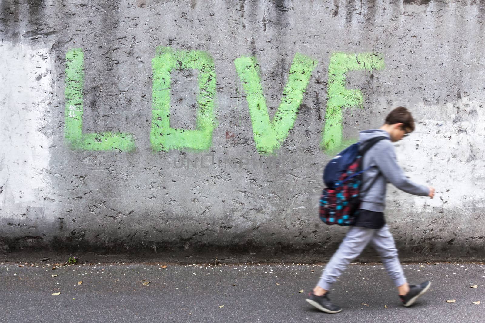 A schoolboy walking down the street with head bowed; on the wall stands the inscription "LOVE".