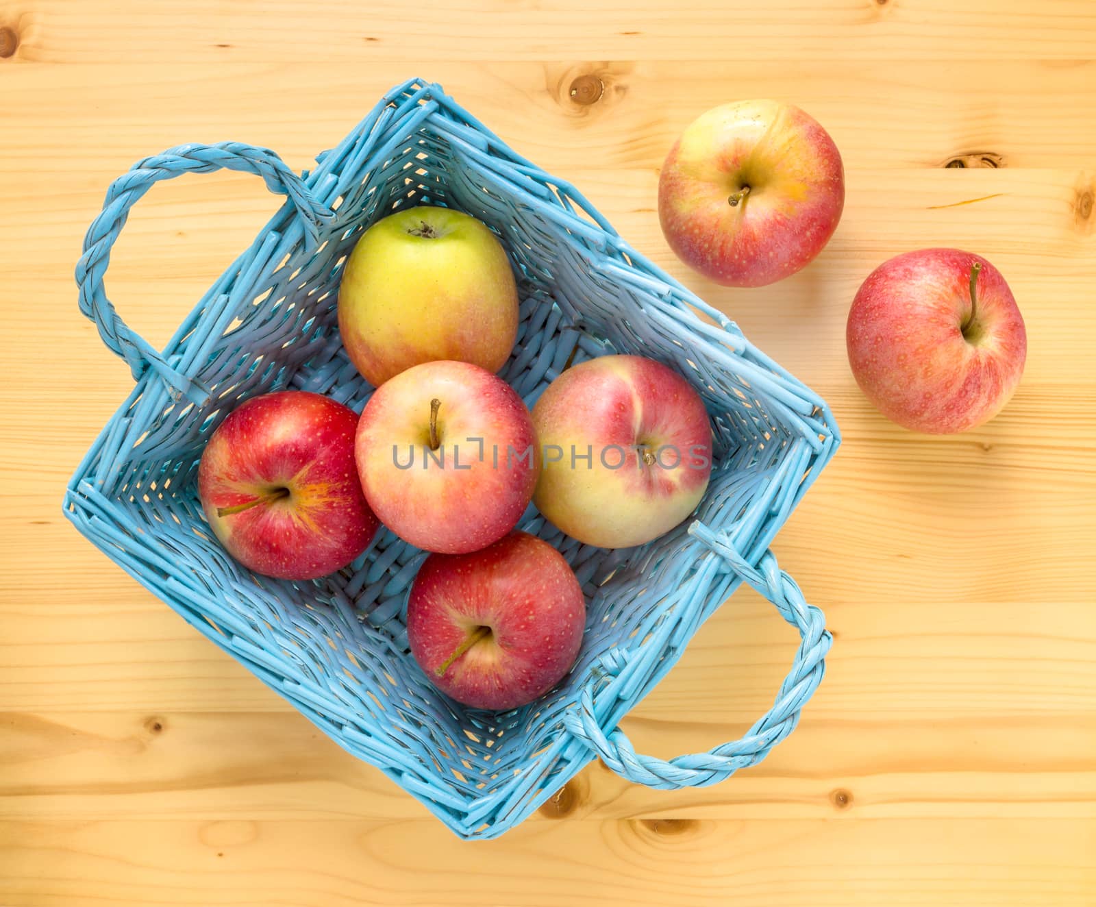 Red apples in blue wooden basket on wooden table. Two apples are remained out of the basket.Top view.