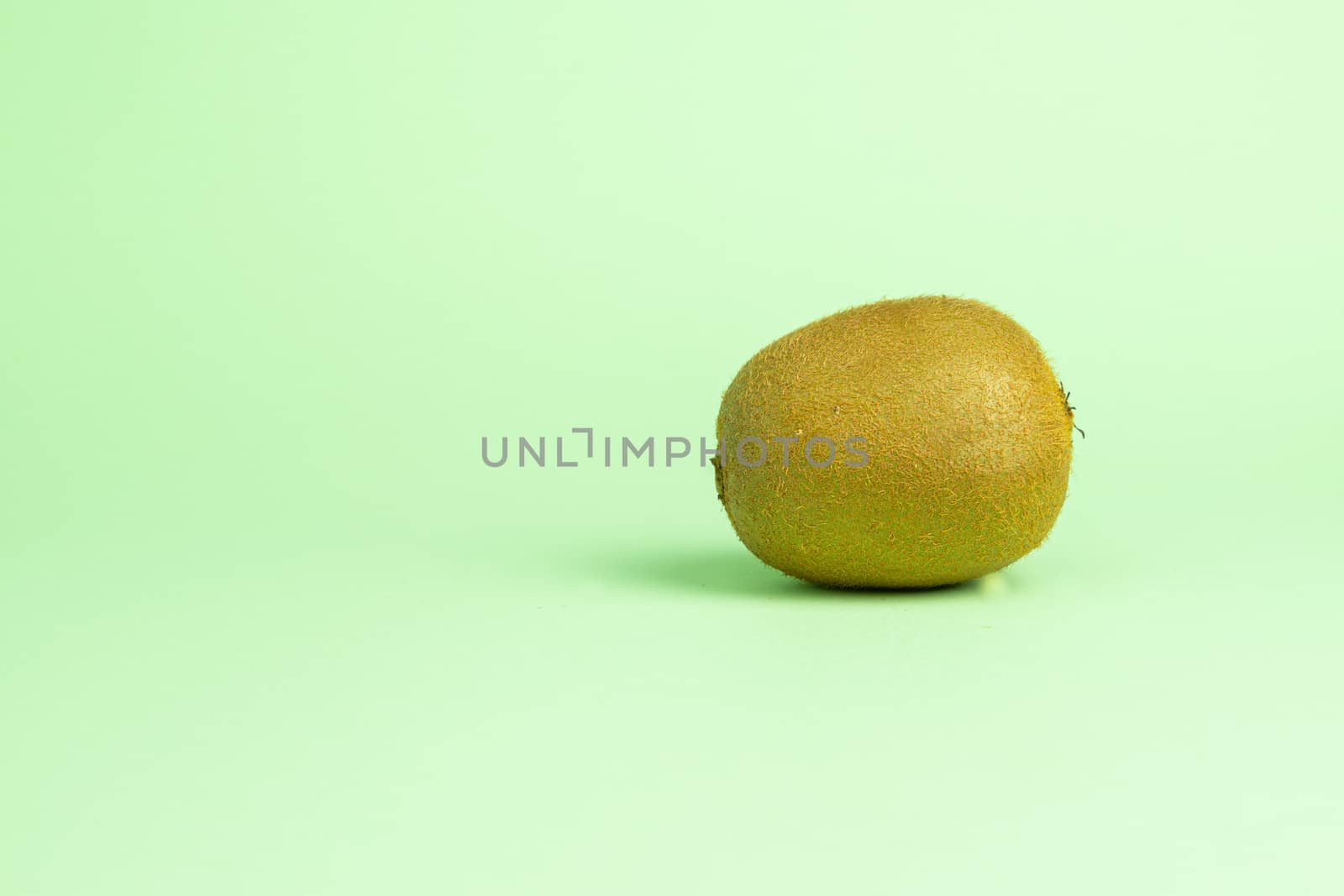 Whole unpeeled ripe kiwi fruit on a turquoise green background on the right