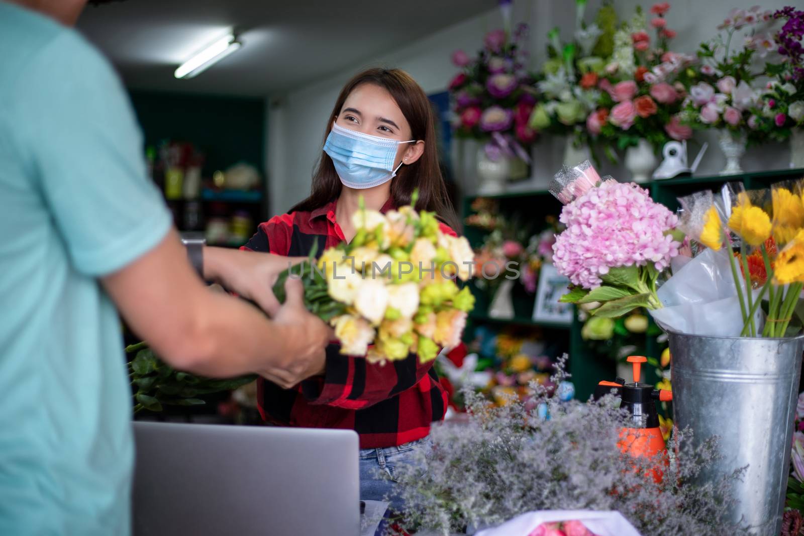 Asian Woman wearing  face mask or protective mask against coronavirus crisis, Florist owner of a small florist business holding flowers for delivery to customers at her store