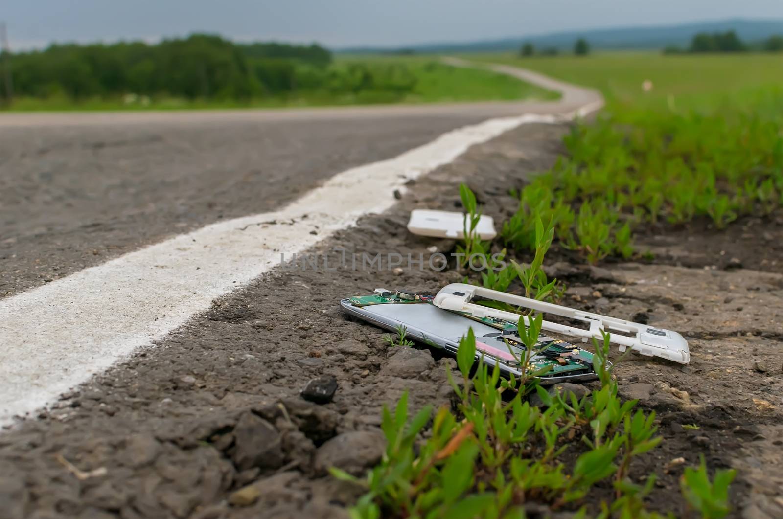 View of a mobile phone lying on the asphalt on a country road in cloudy weather