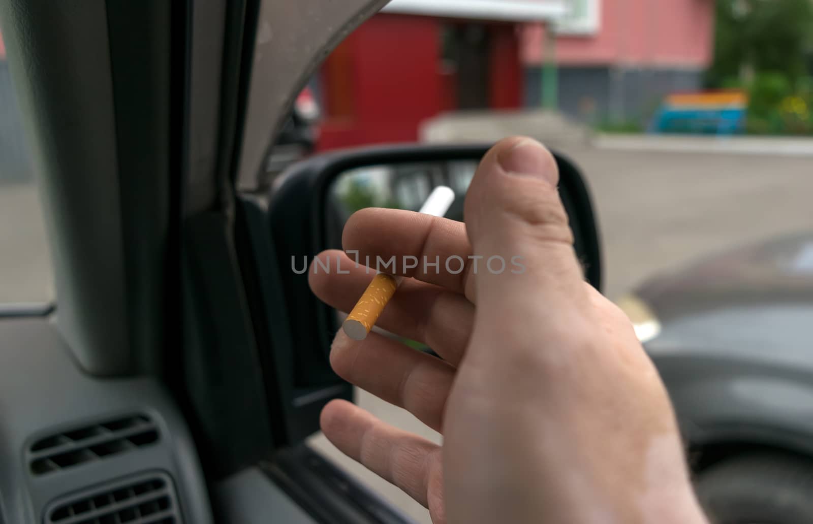 close-up of a cigarette in the hand of a man in the car, who watches the entrance door of the house