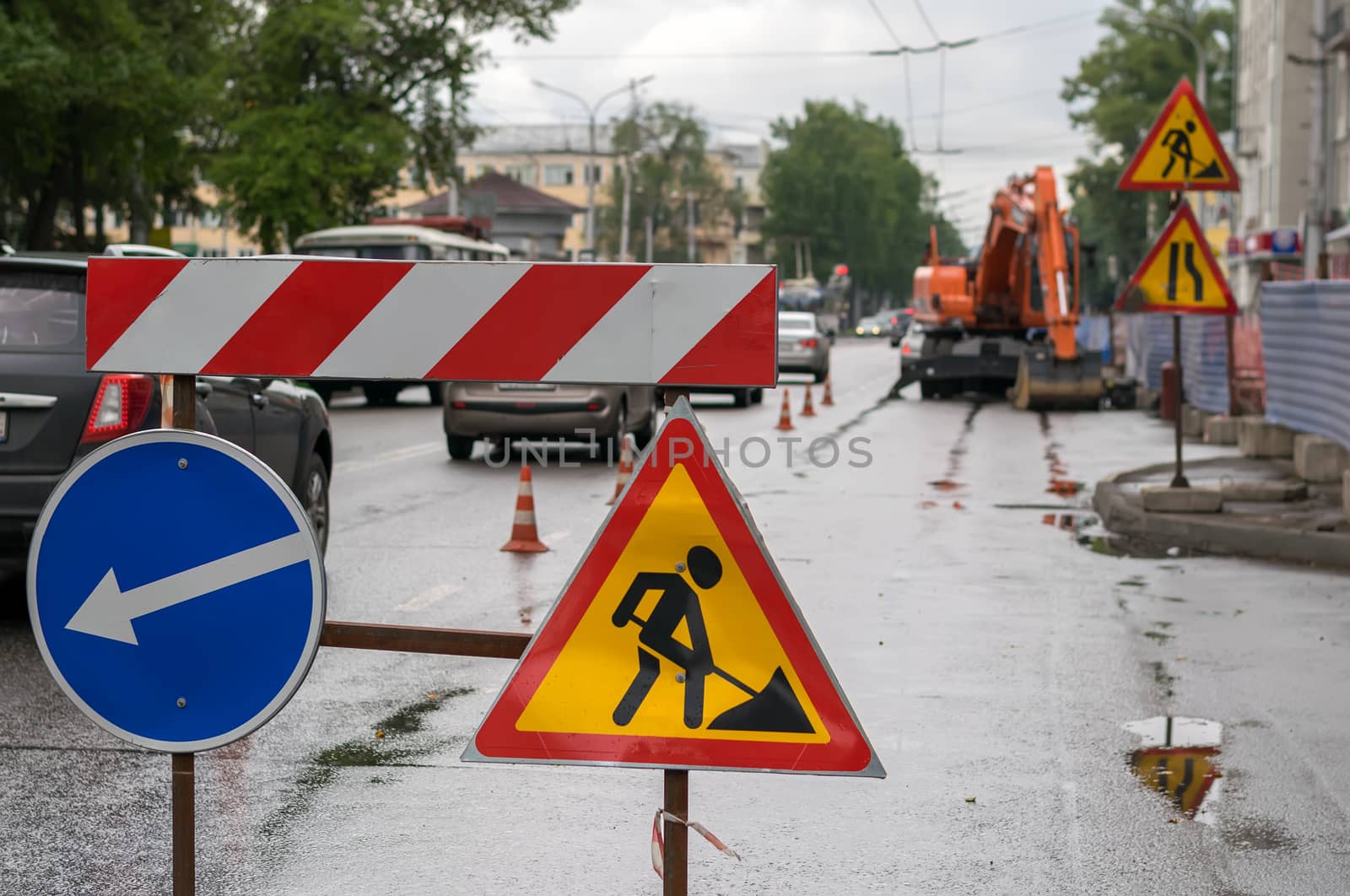 Traffic signs, detour, road repair on the background of the street and the excavator who digs the pit