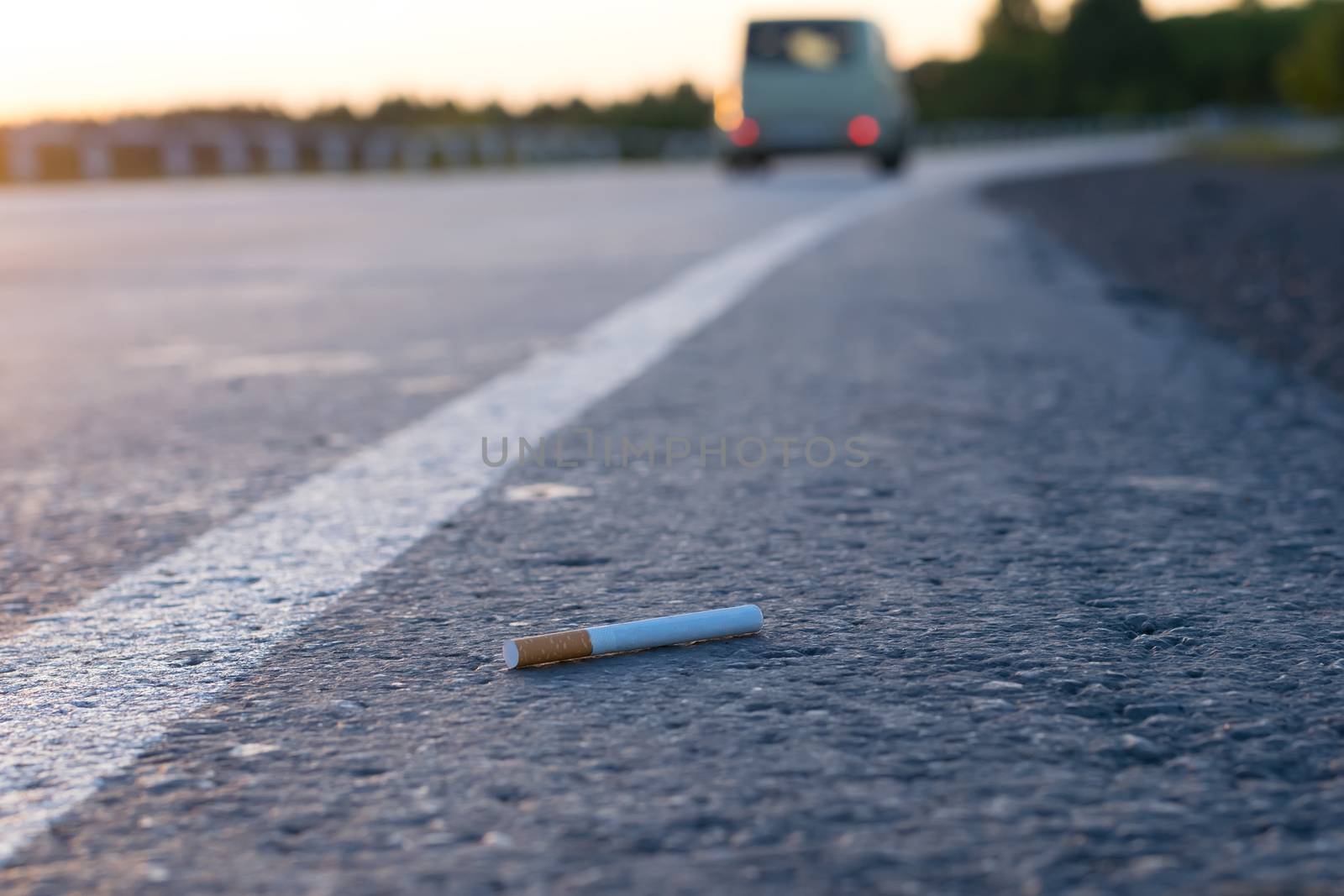 view of cigarette lying on the asphalt on a country road by jk3030
