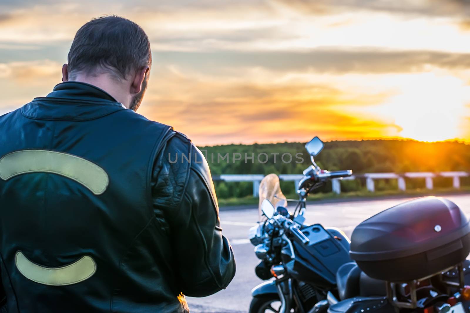 biker in a leather jacket standing next to the motorbike by jk3030