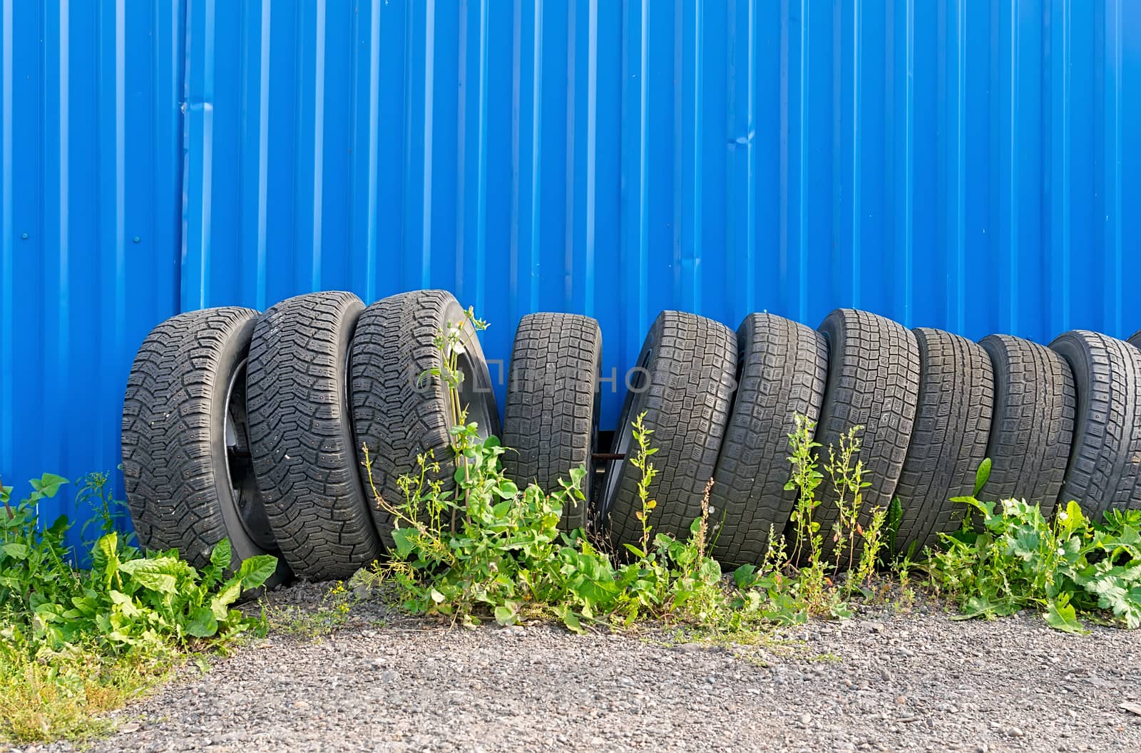 sets of car tires with disks are on the street on the ground near the fence of the cottage