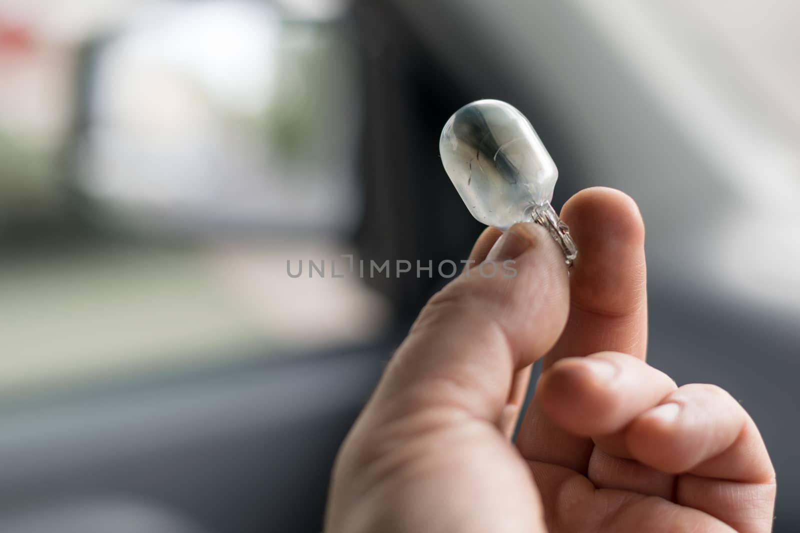 the fingers of the human hand hold the damaged light bulb in the car by jk3030
