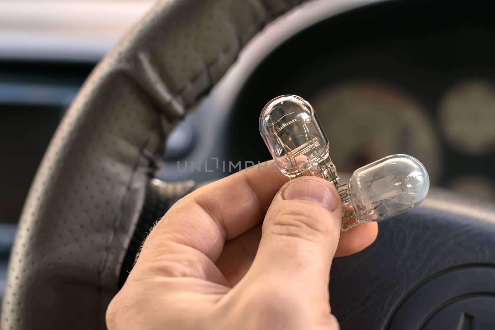 new and burnt out car light bulb, in man's hand by jk3030