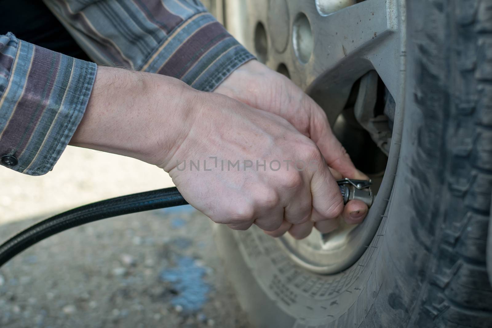 human hands insert the hose of the car pump to pump air into the wheel of the car