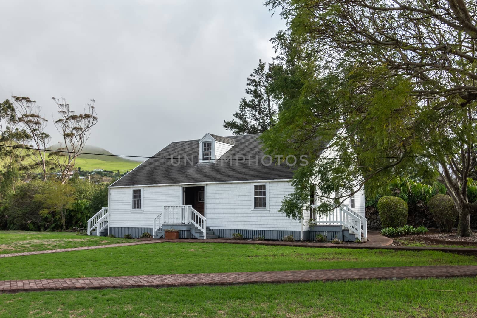 Waimea, Hawaii, USA. - January 15, 2020: Parker Ranch headquarters. White wooden house surrounded by green trees behind green lawn and under light blue cloudscape.