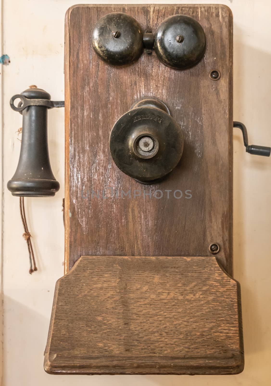 Waimea, Hawaii, USA. - January 15, 2020: Parker Ranch headquarters. Old telephone has metal bell, hear piece and handle to turn, all on brown wooden plank, fixed to beige wall.