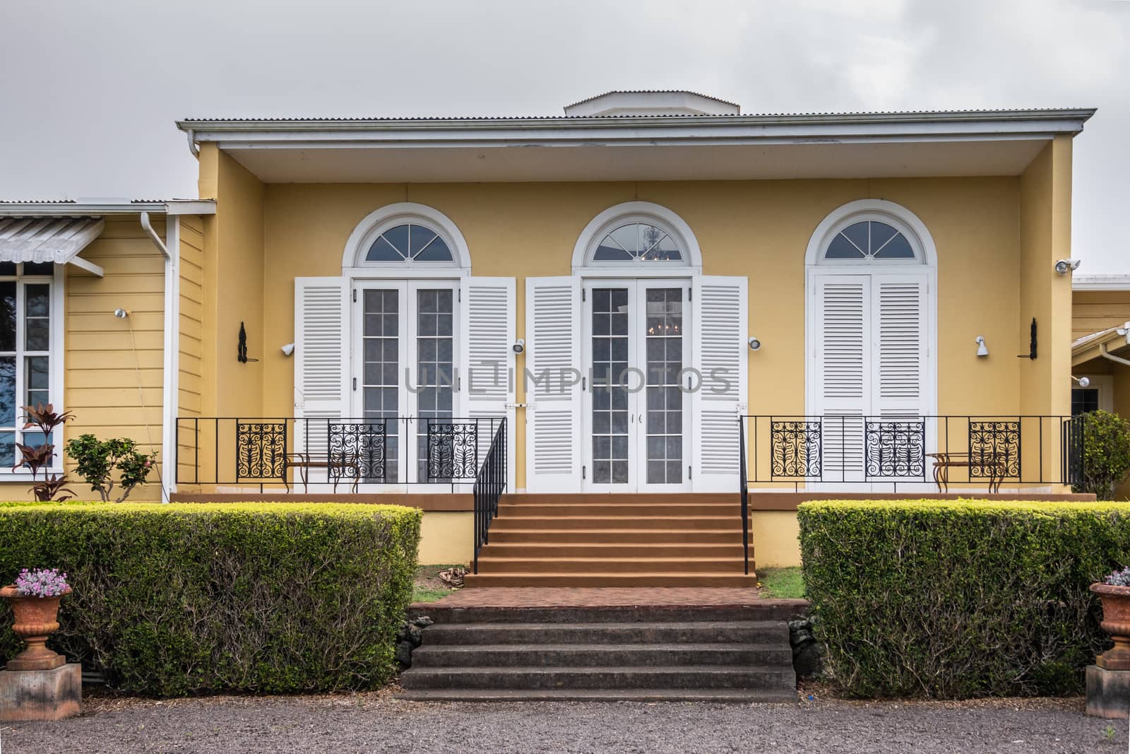 Waimea, Hawaii, USA. - January 15, 2020: Parker Ranch headquarters. Yellow walls with white window frames and shutters of wing of main house. Green hedge and stairs in fornt. Silver sky.